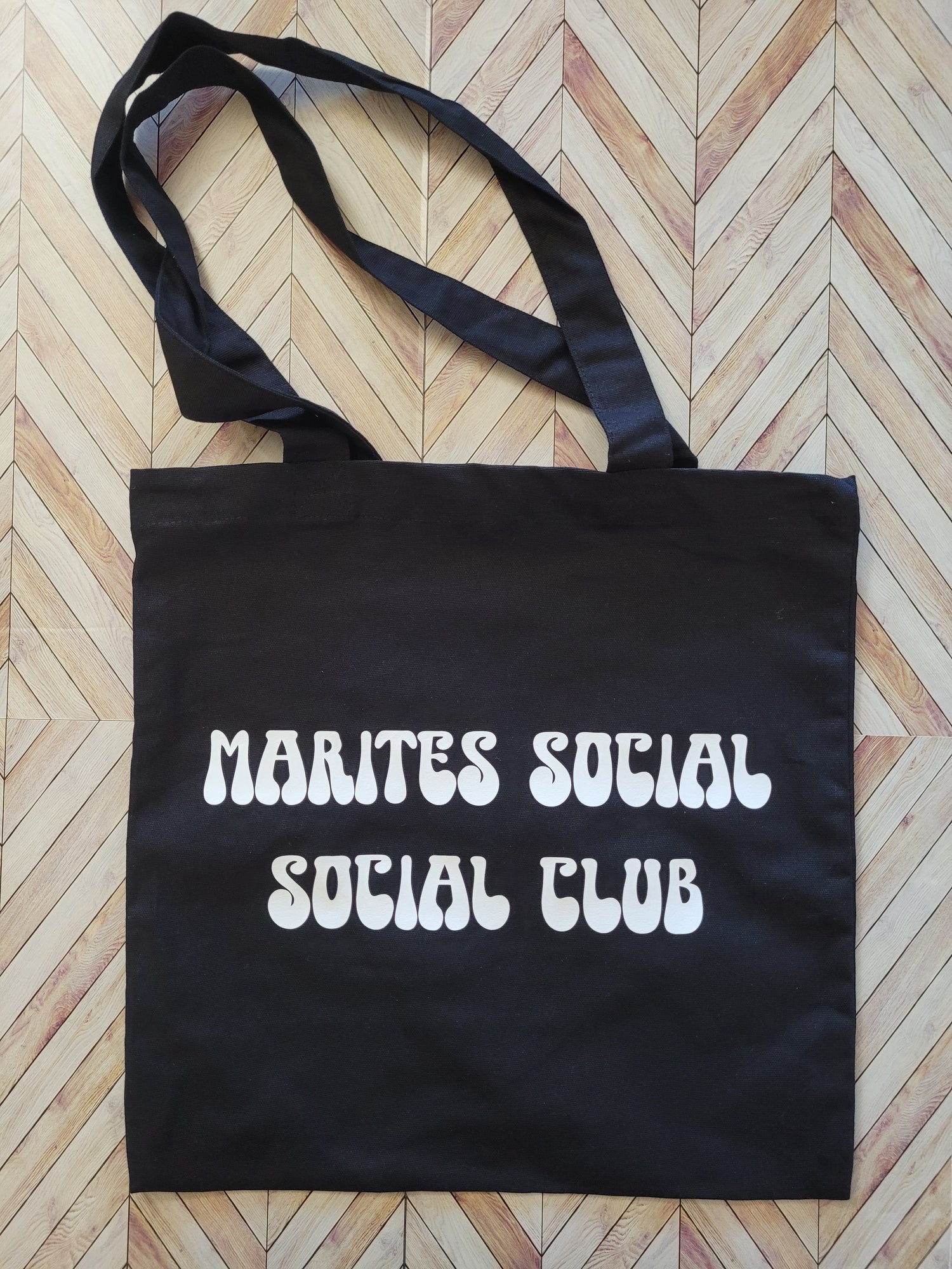 Black tote bag with 'Marites Social Club' text on a wooden floor